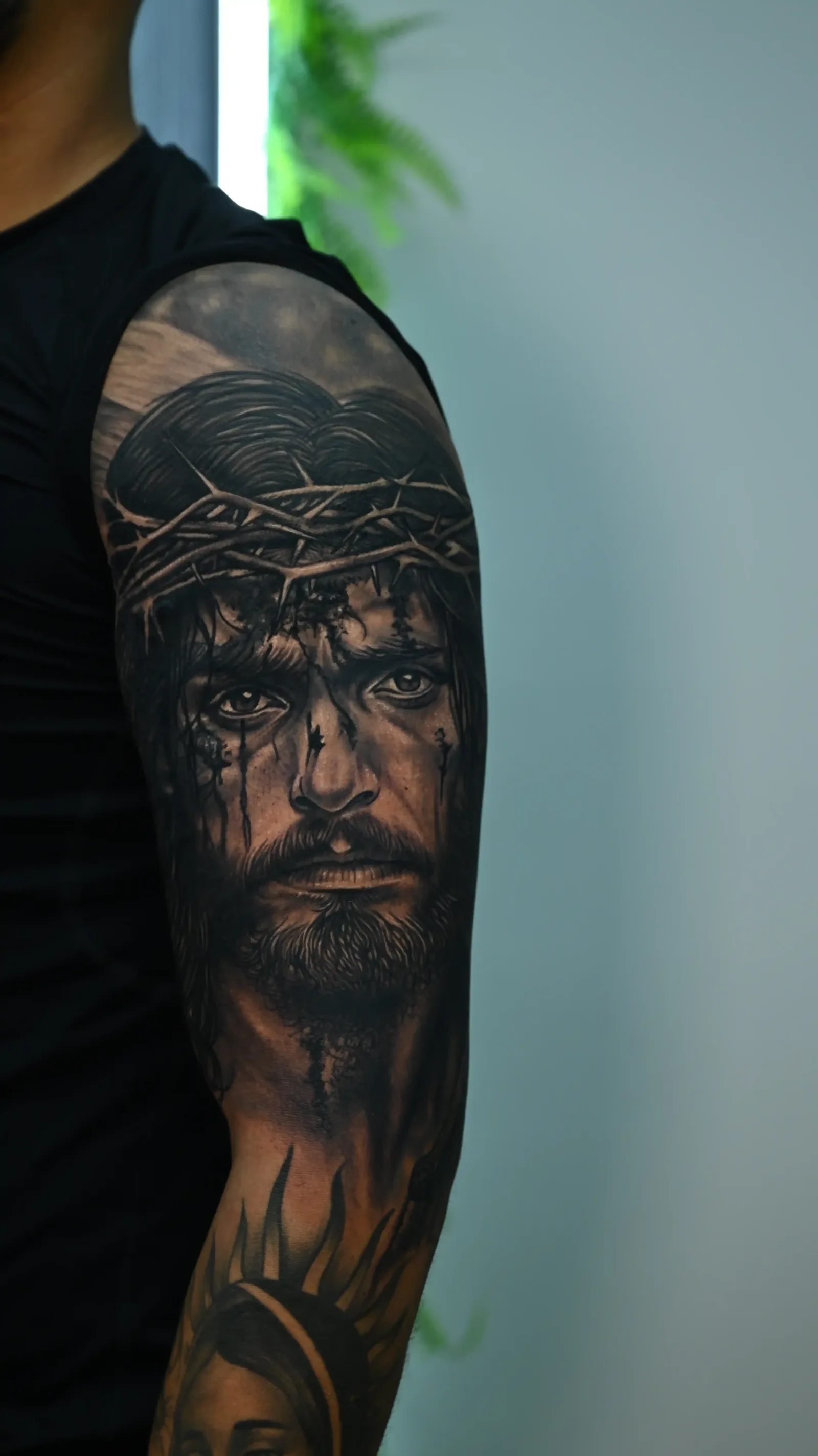 Black and grey realism upper-arm sleeve of Christ with crown of thorns by Danyi at Shadow Studio Charlotte