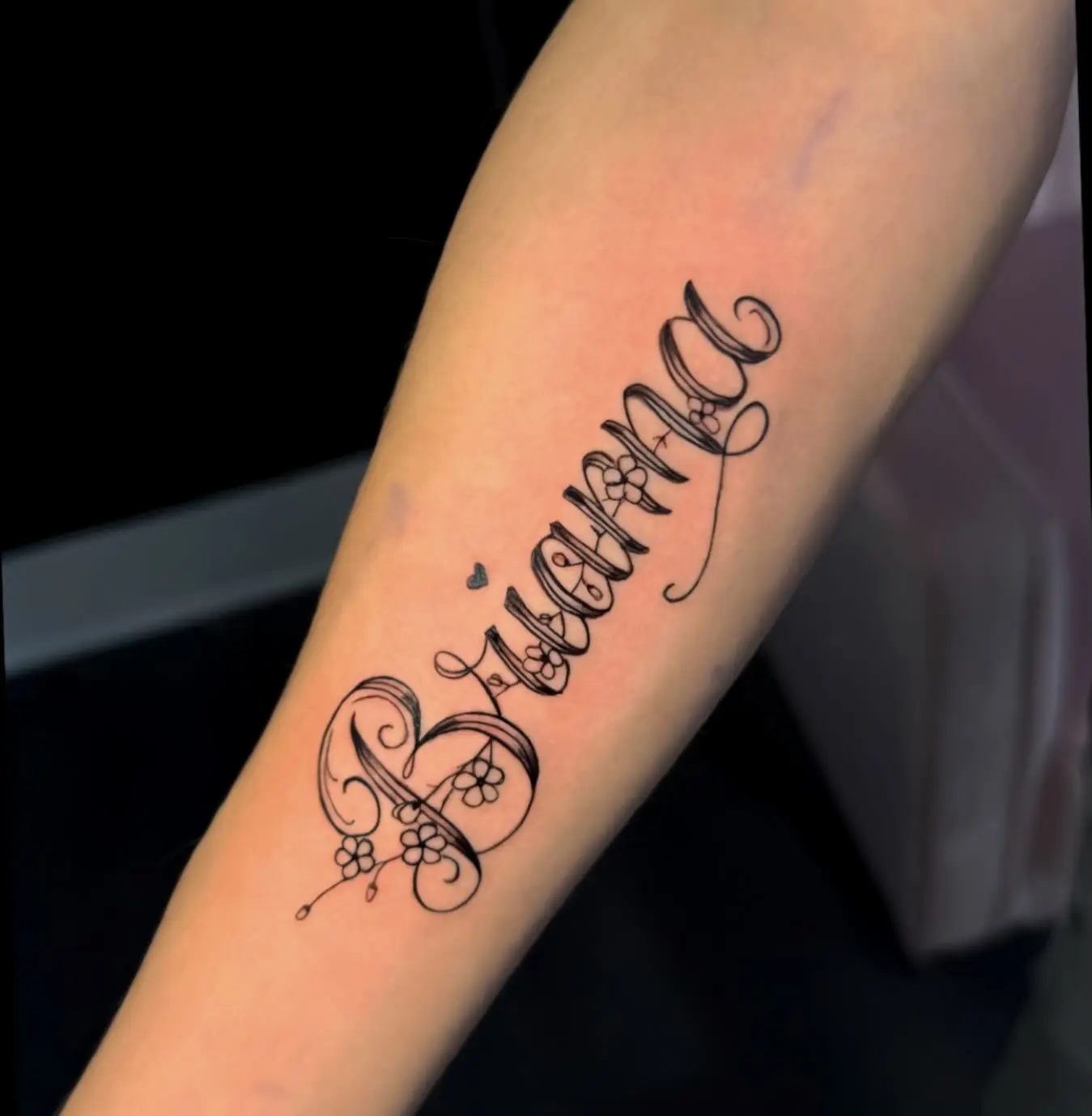 Fine line "Brianna" script forearm tattoo with floral accents by Venus at Shadow Studio Charlotte